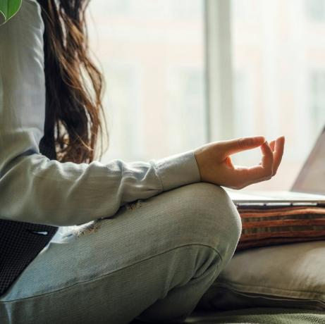 una donna asiatica di mezza età in blue jeans seduta sul letto in una posa yoga davanti a un laptop che lavora a distanza a casa facendo acquisti online durante il periodo di quarantena