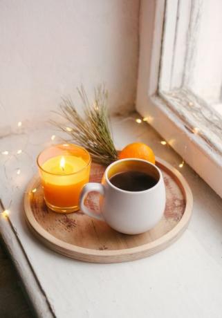 accoglienti dettagli interni della casa invernale, tazza di caffè, vassoio in legno, mandarino e candela davanzale ancora in vita per natale