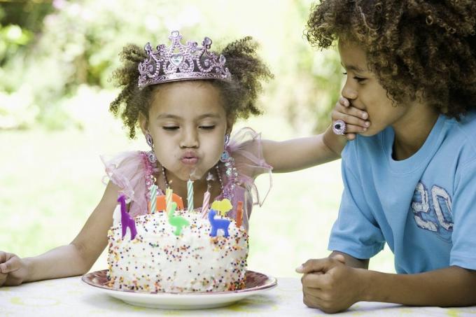 ragazza carina con la corona che spegne le candeline e copre la bocca del fratello