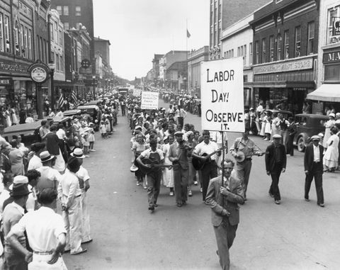 parata della festa del lavoro nel 1934 con persone che camminano per strada tenendo cartelli mentre una folla guarda dai marciapiedi