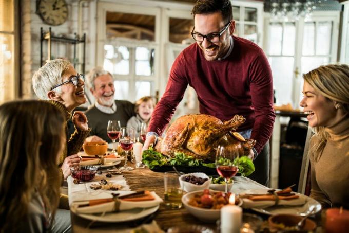 uomo felice che serve tacchino arrosto alla sua famiglia durante la cena del ringraziamento al tavolo da pranzo