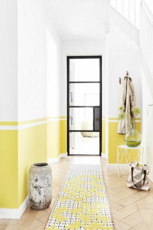 corridoio con una porta con cornice nera, le pareti sono dipinte di giallo a metà della linea di fondo, un uso attento di nastro adesivo e un la livella è la chiave per creare questo effetto di pittura lineare, dipingi ogni sezione a turno e lasciala asciugare prima di passare alla successiva uno