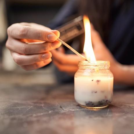 raccolto donna anonima con fiammifero acceso candela aromatica in vaso di vetro posto sul tavolo di marmo a casa