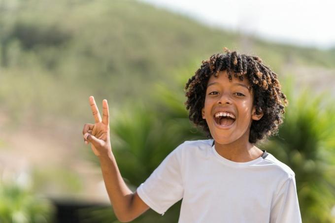 Un ragazzo afroamericano di 10 anni che ride ad alta voce mentre fa il segno della pace