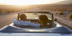 vista posteriore della coppia in viaggio alla guida di un'auto classica convertibile verso il tramonto