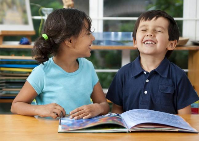 due bambini che ridono godendo di un libro a scuola