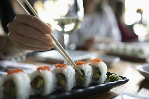 Donna con le bacchette che raggiungono per i sushi sul vassoio del ristorante