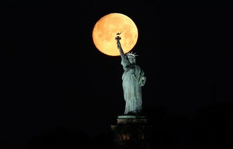 La luna tramonta dietro la statua della libertà a New York City