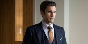 wes bentley in un completo grigio scuro a tre pezzi con una cravatta stampata marrone e una camicia a righe bianche e blu in piedi in un ufficio con le mani in tasca