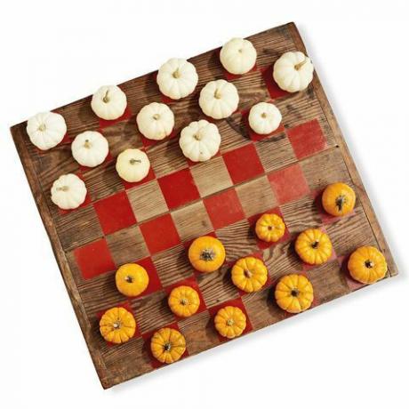 una tavola di legno dipinta come un gioco di dama usando mini zucche bianche e arancioni come pedine