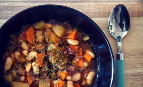 Zuppa di fagioli bianchi con cipolla, carota, patate e verdure varie in un piatto nero con un po 'di prezzemolo in cima e cucchiaio sul lato.