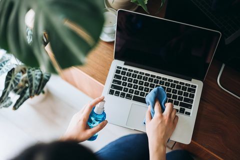 foto ritagliata di una giovane donna che pulisce la superficie del laptop con spray detergente e panno antistatico a casa