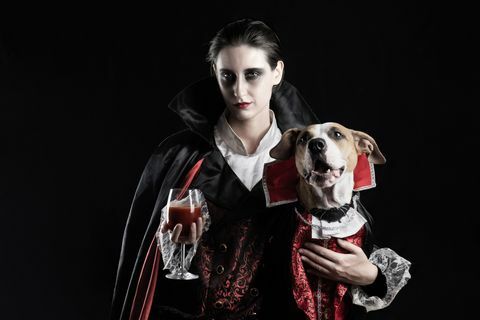 Giovane donna con un bicchiere di bevanda rossa e il suo cucciolo vestito con lo stesso costume di Draculacula