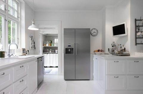 Cucina bianca con frigorifero verticale argento nella ristrutturazione della casa di Hanne Davidsen, Silkesborg, Danimarca.