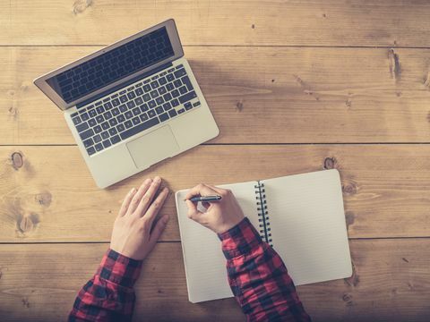 colpo dall'alto di un uomo che scrive in un blocco note con un laptop accanto a lui