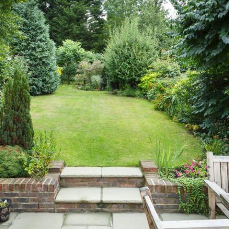 Giardino sul retro terrazzato e paesaggistico in Inghilterra, Regno Unito, con patio, erba e gradini in pietra