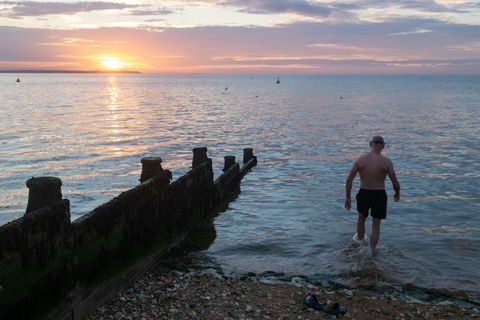 mentre il sole tramonta sulla luce del giorno sbiadita e sulle calme acque dell'estuario del Tamigi, un selvaggio nuotatore entra in acqua per il suo tuffo serale regolare, il 18 luglio 2020, a whitstable, kent, inghilterra foto di richard baker in immagini tramite getty images