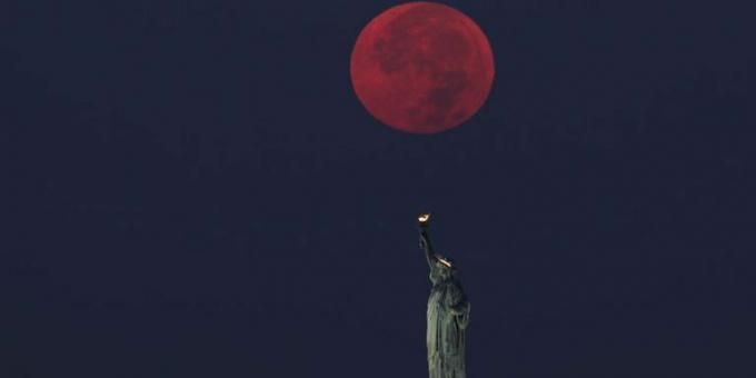 la luna piena tramonta dietro la statua della libertà a new york city