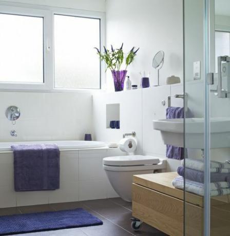 Bagno luminoso con asciugamano viola sul lato del bagno e asciugamani piegati vicino alla doccia